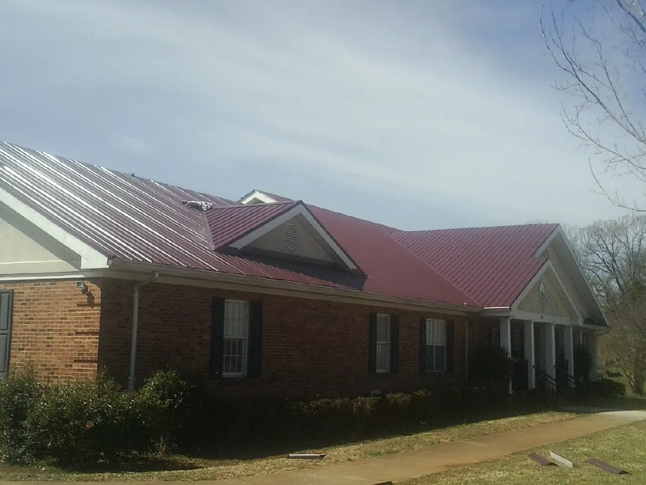 Red metal roof with gabled entries on a long brick building, from a Hail Damage Roof Repair job in Sandisfield