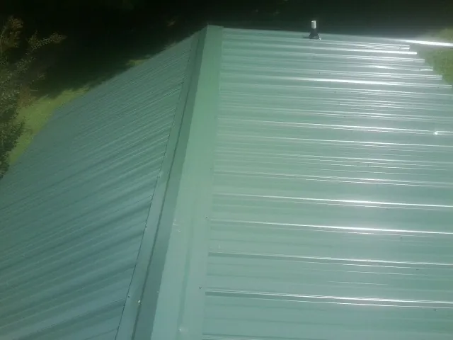 New green metal panels meeting at the ridge of a roof — Flat Roof Repair work by our crew in Sandisfield