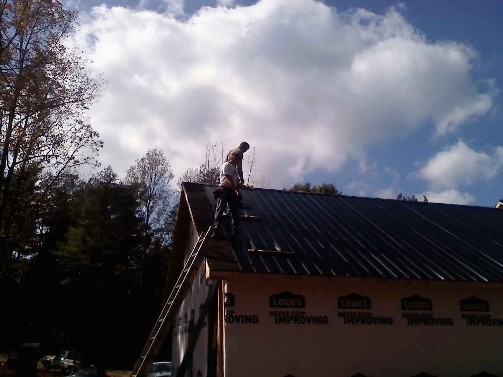 Roofer fastening dark metal panels high against a cloudy sky, from a Roof Inspection job in Sandisfield