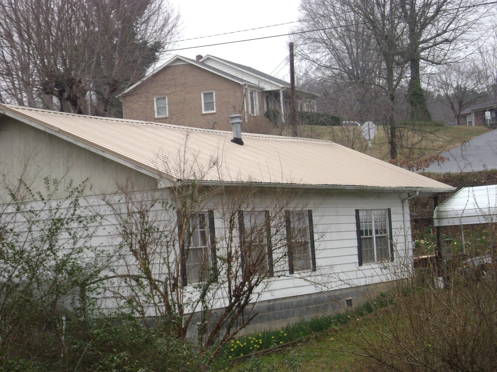 Tan metal roof on a white sided house set into a hillside — Commercial Roofing by Roofing Brothers in Sandisfield